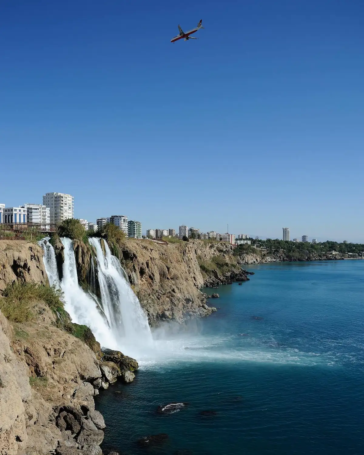 The Lower Duden waterfalls plunging off a rocky cliff into the Mediterranean Sea with the city behind