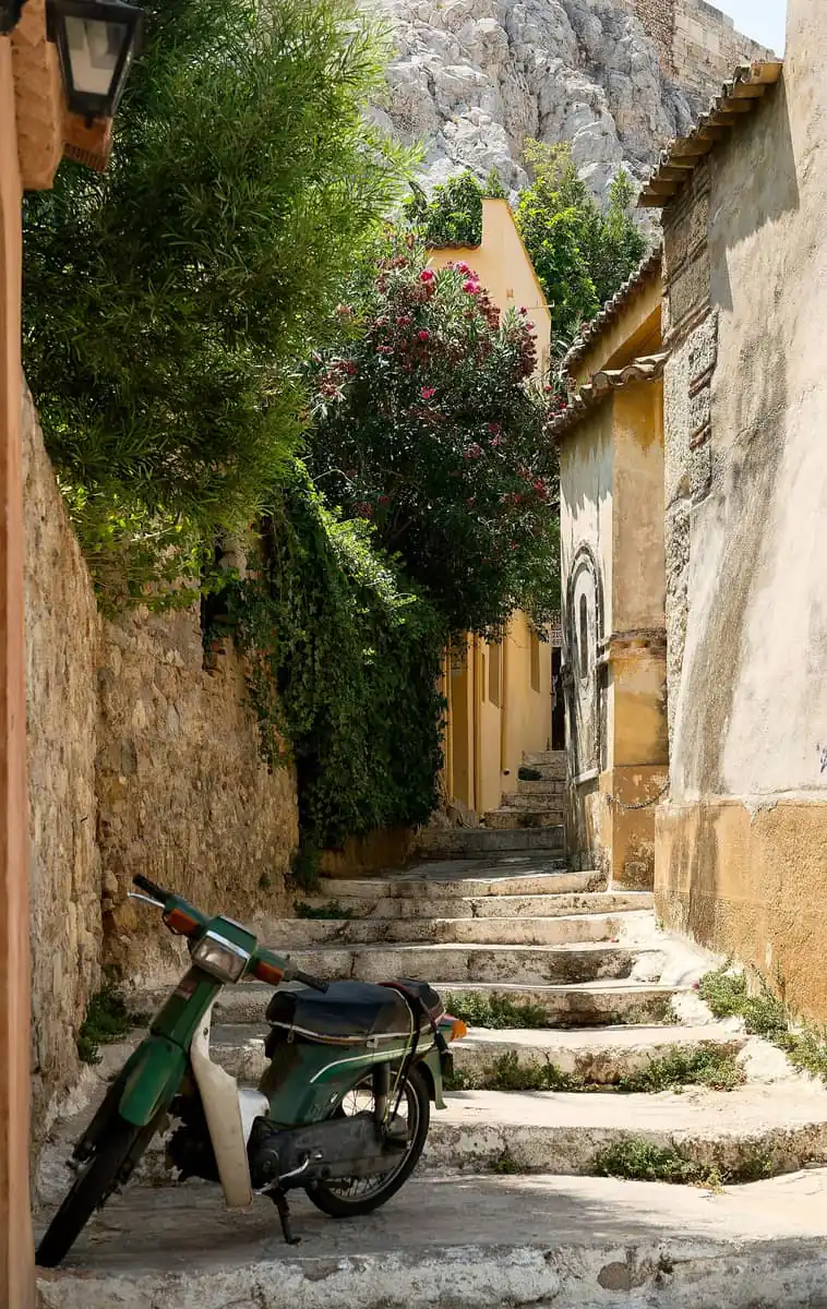 A stepped lane in Anafiotika above Plaka, with a scooter parked on the steps and the rock above