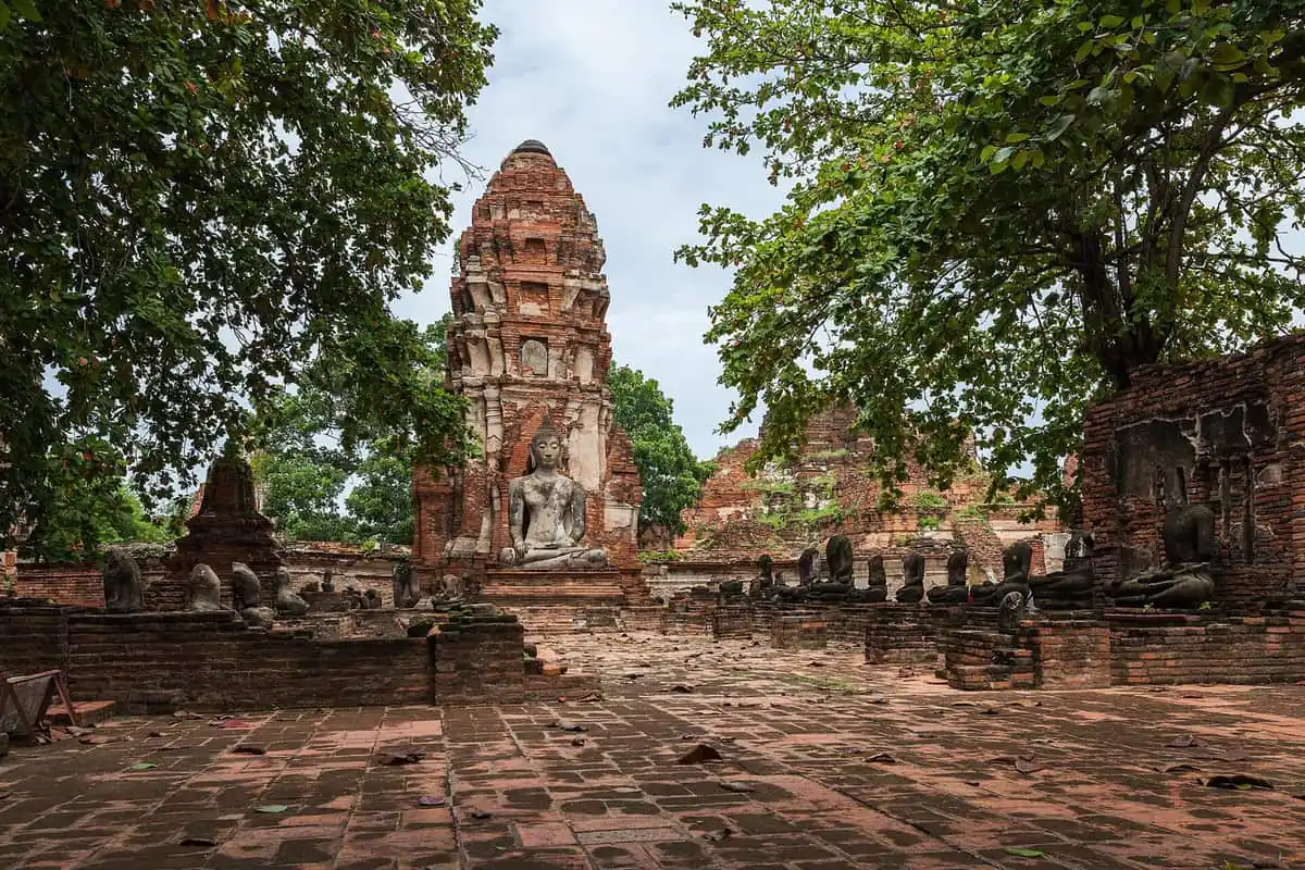A seated Buddha and rows of headless statues among brick ruins at Wat Mahathat in Ayutthaya