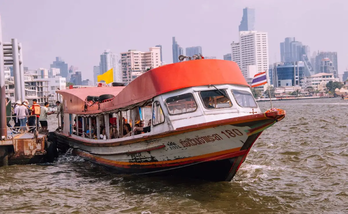 A Chao Phraya Express Boat arriving at a pier, with the Bangkok skyline behind