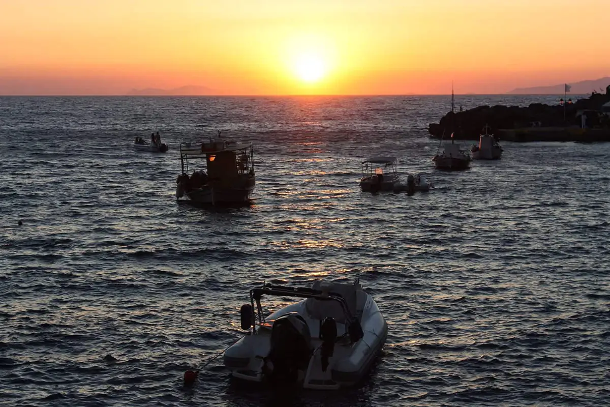 Fishing boats anchored off the port below Oia, Santorini, at sunset