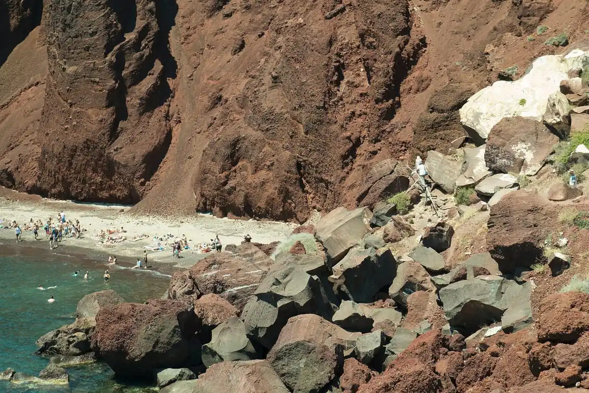 Swimmers and sunbathers below the red cliffs of Red Beach on Santorini