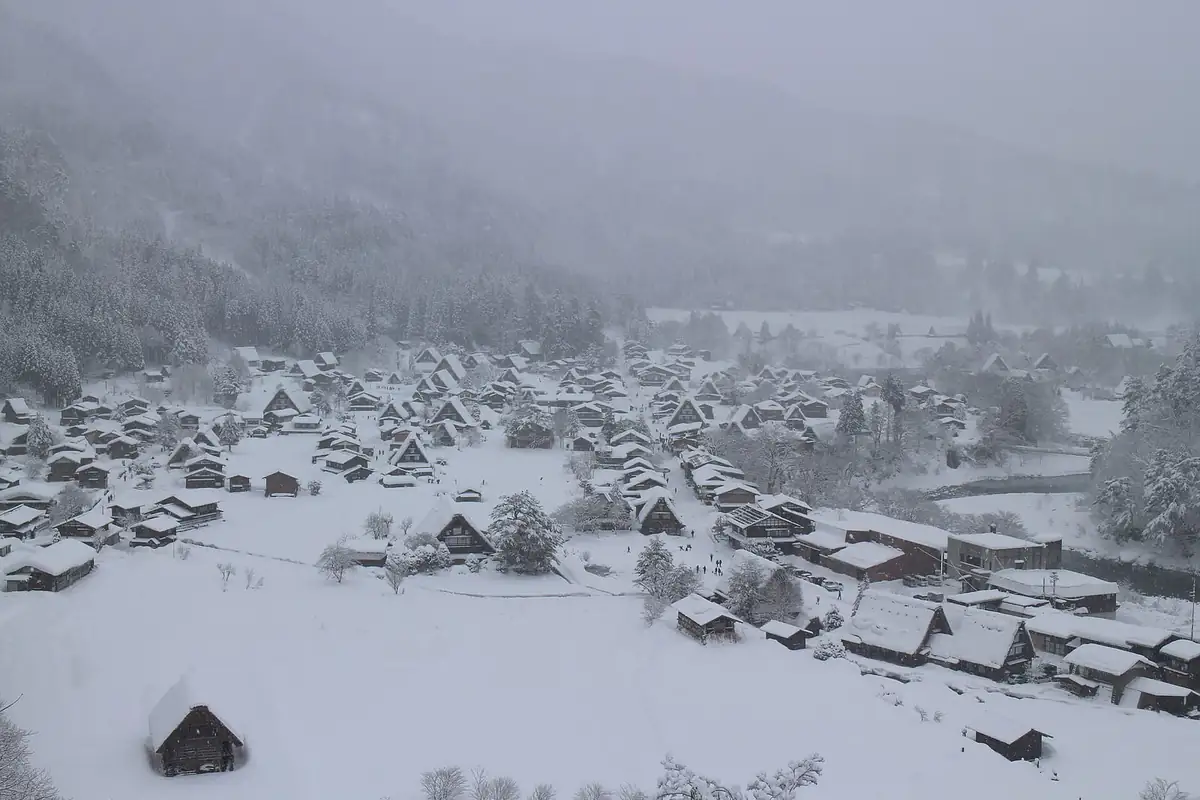 Thatched-roof houses of Shirakawa-go village blanketed in deep snow with forested mountains behind