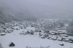 Thatched-roof houses of Shirakawa-go village blanketed in deep snow with forested mountains behind