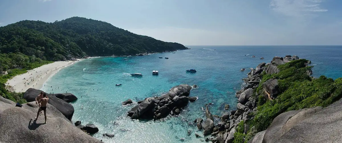 Turquoise bay and white beach on the Similan Islands seen from granite boulders, with tour boats anchored offshore