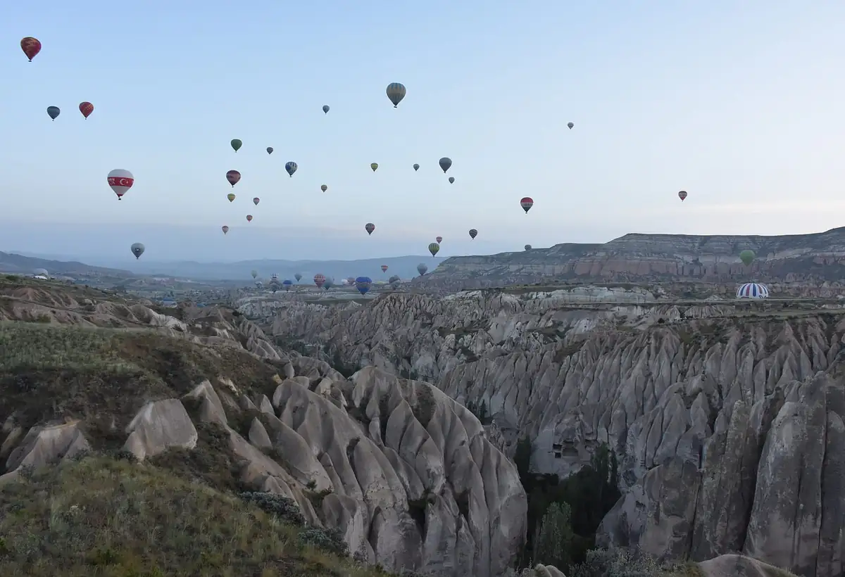 Dozens of hot air balloons rising over eroded rock valleys near Goreme at dawn