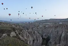 Dozens of hot air balloons rising over eroded rock valleys near Goreme at dawn