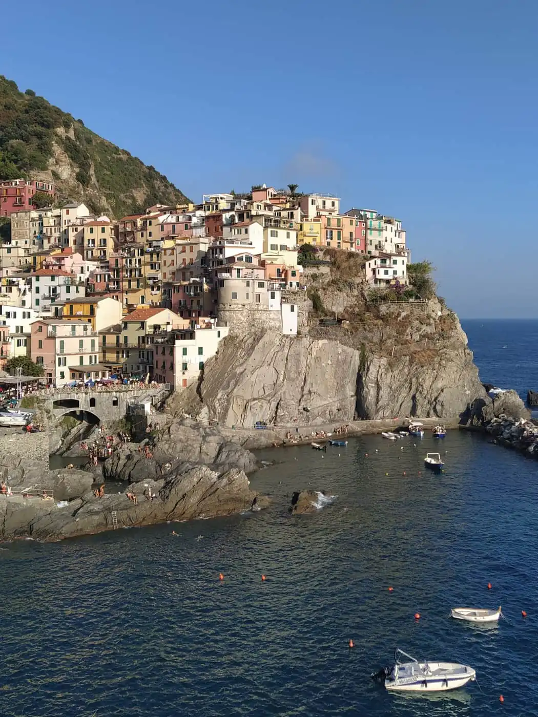 Manarola's pastel houses on a rock above the sea with small boats in the harbour