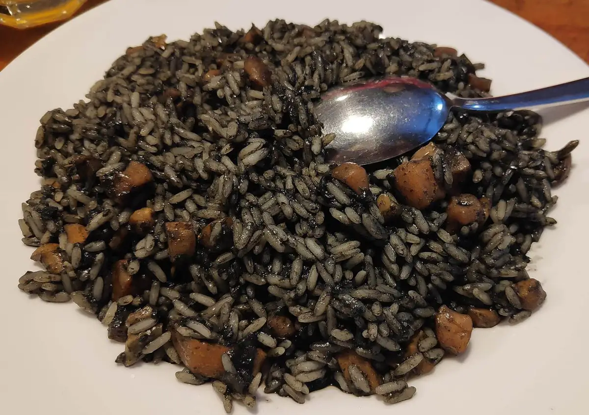 A plate of black cuttlefish risotto with a spoon