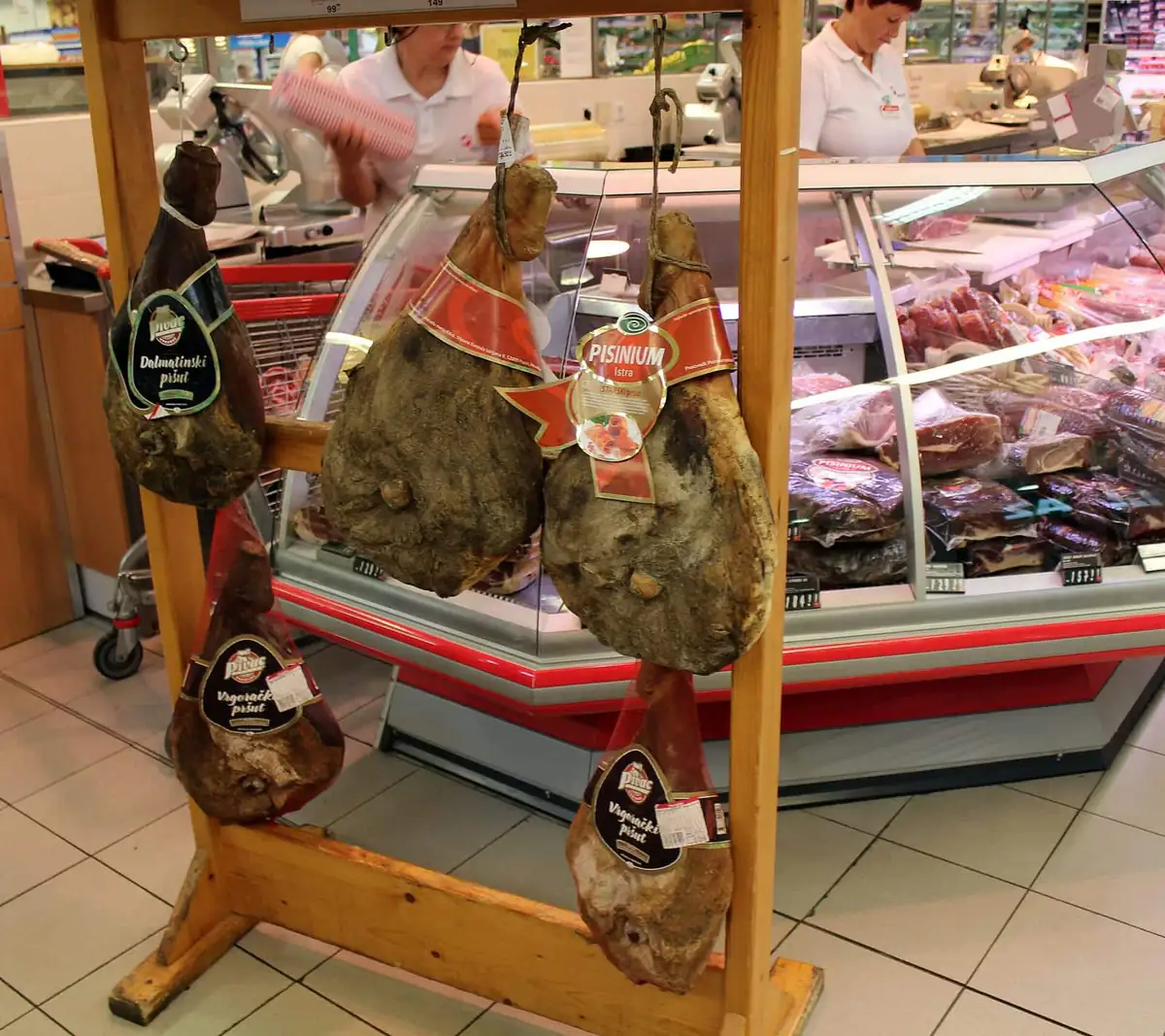 Cured pršut hams hanging at a deli counter