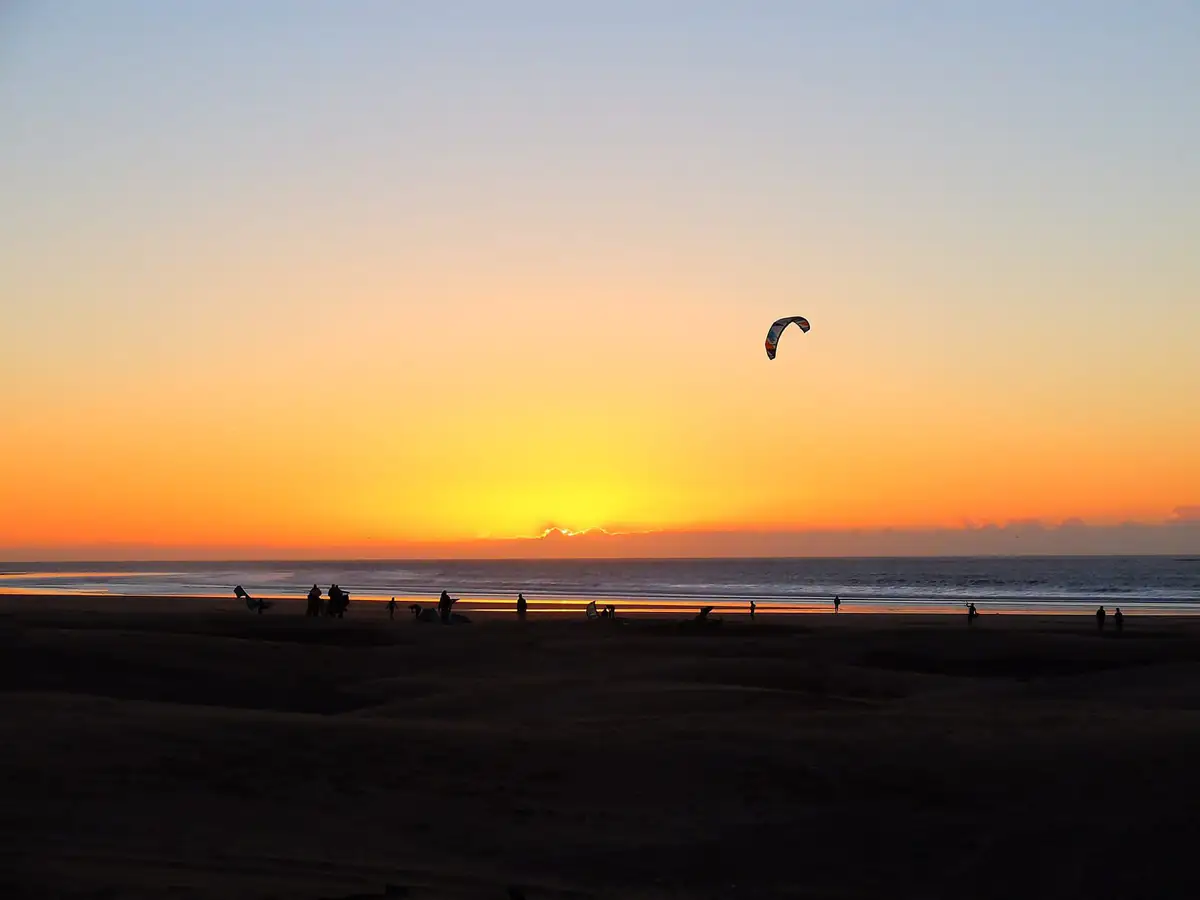A kitesurf kite against an orange sunset over the beach at Essaouira