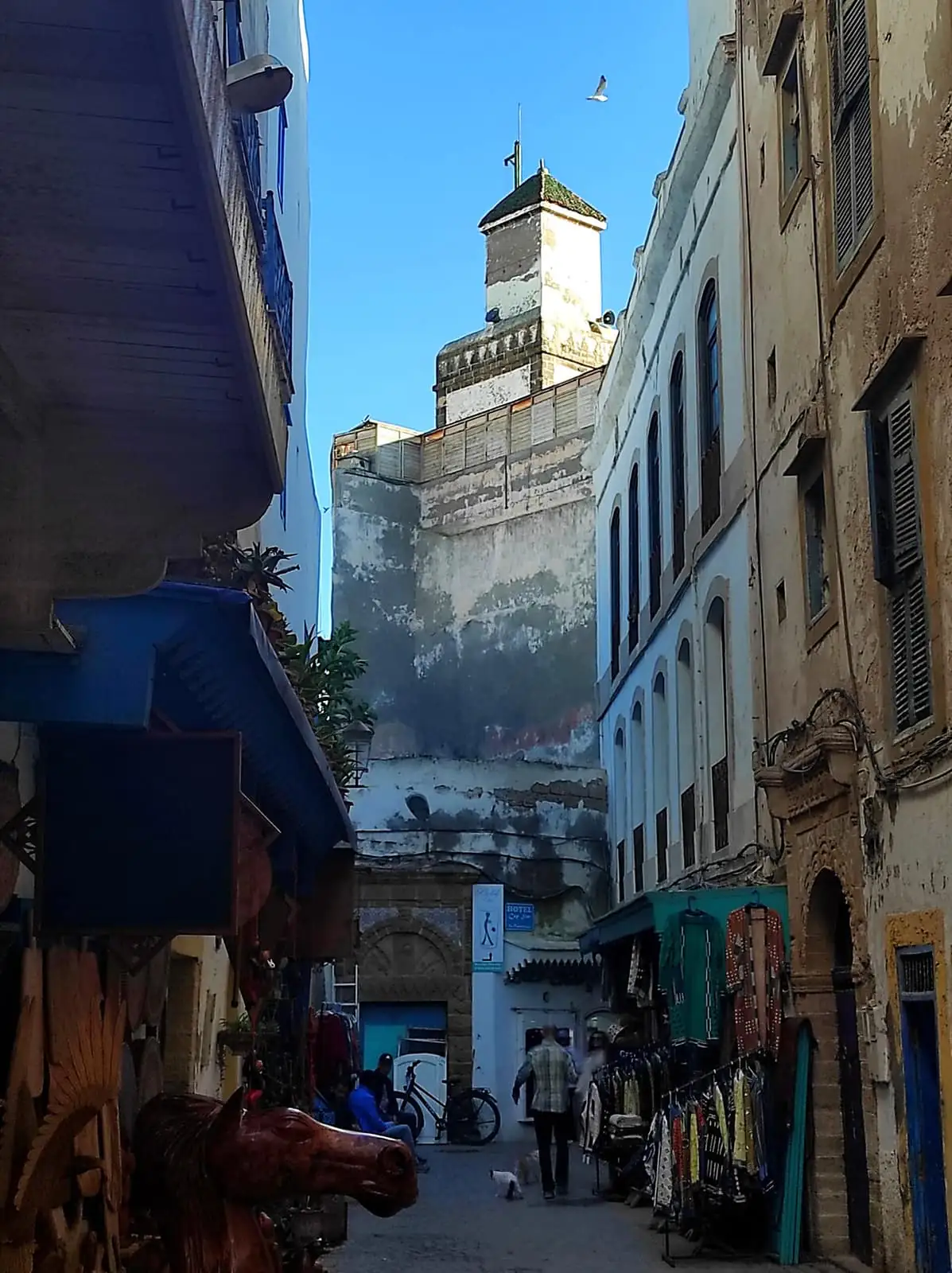 A whitewashed medina street in Essaouira with a fortified tower and blue shutters