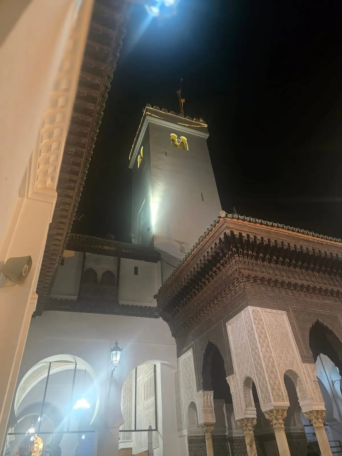 The minaret of the Al-Qarawiyyin Mosque lit up at night, seen from a nearby courtyard