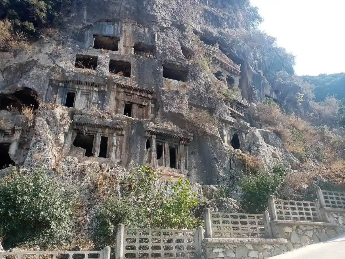 Lycian rock tombs carved into the cliff face above Fethiye, with carved doorways and a road at the foot of the rock