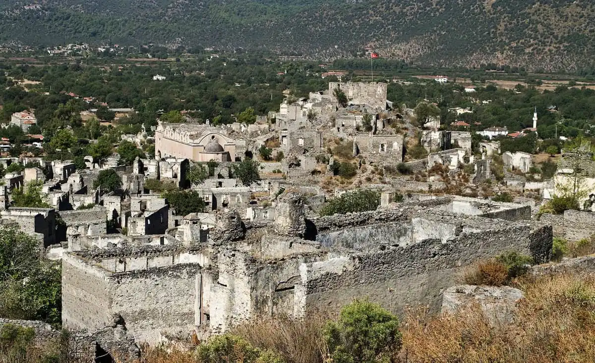The abandoned stone houses and churches of Kayaköy spread across a hillside below wooded mountains