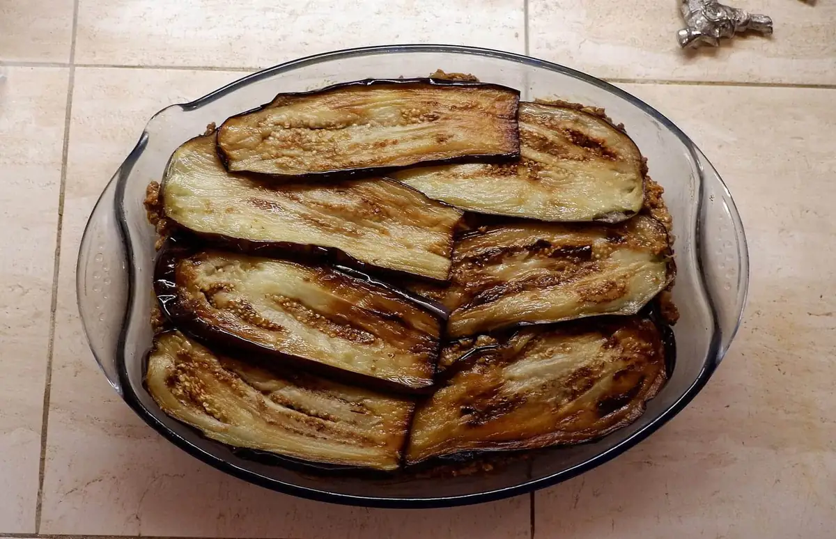 Sliced aubergine layered over mince in a glass dish of moussaka before baking