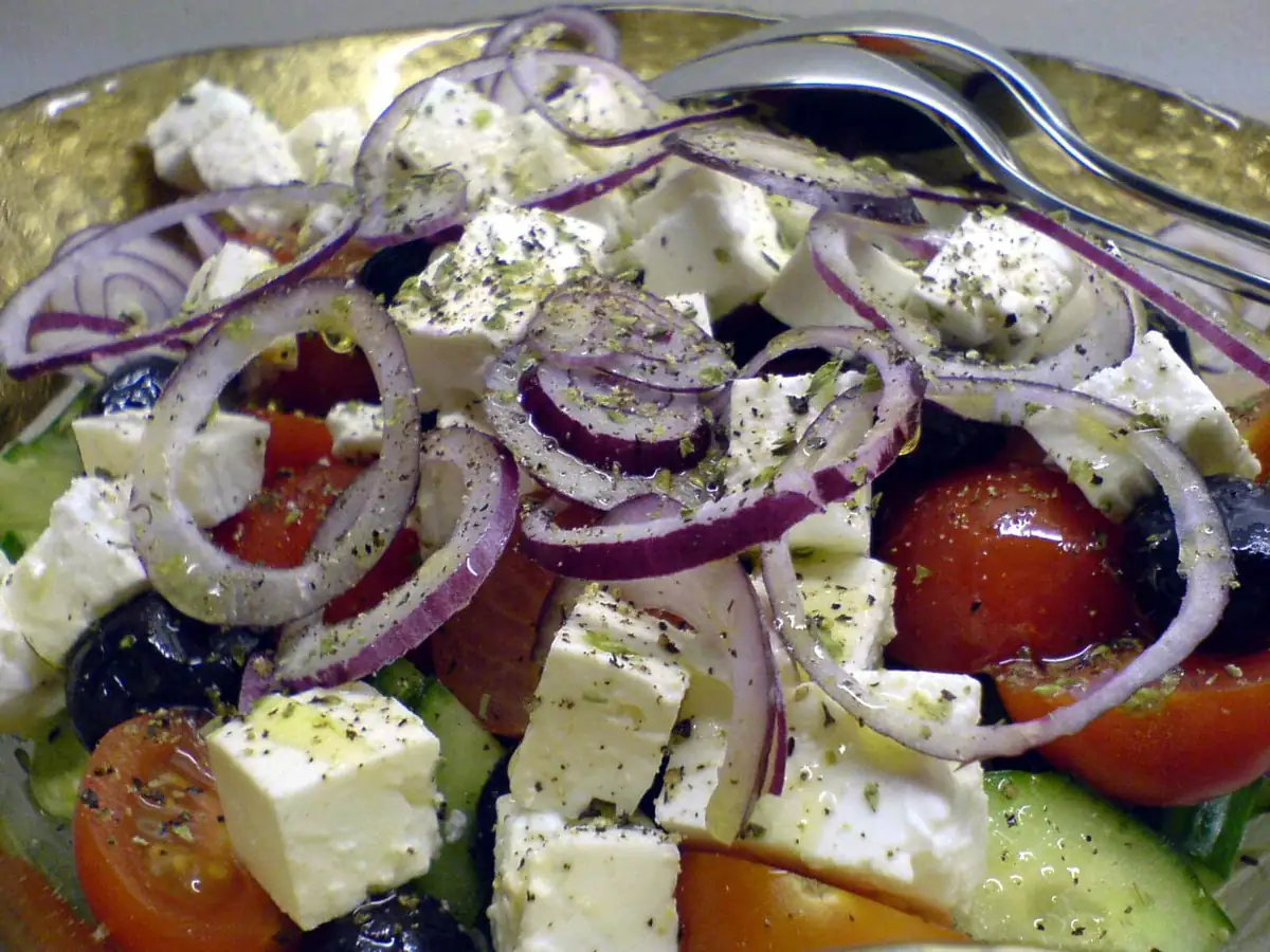 A Greek salad topped with cubed feta, red onion rings, tomatoes, olives and cucumber