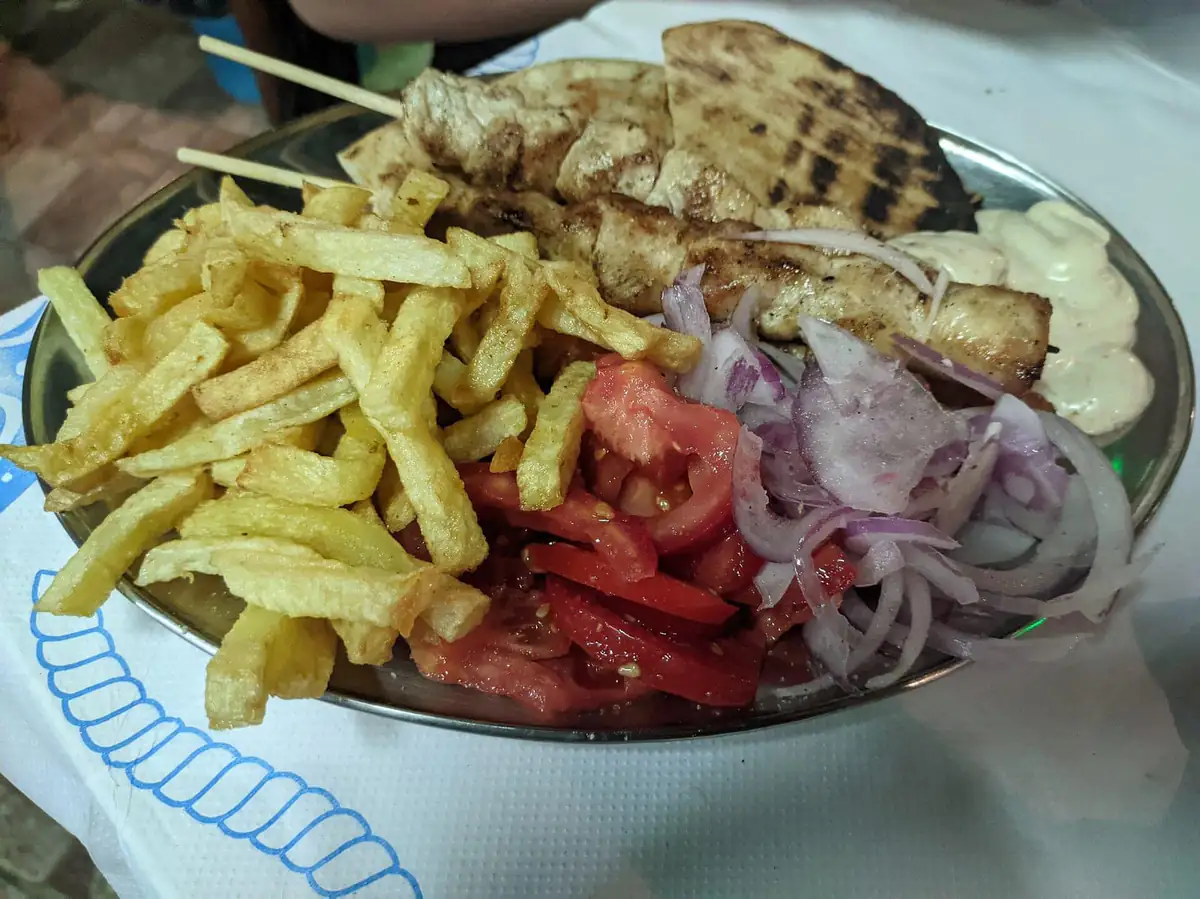 A plate of chicken souvlaki skewers with chips, pita, tomato and onion at a taverna