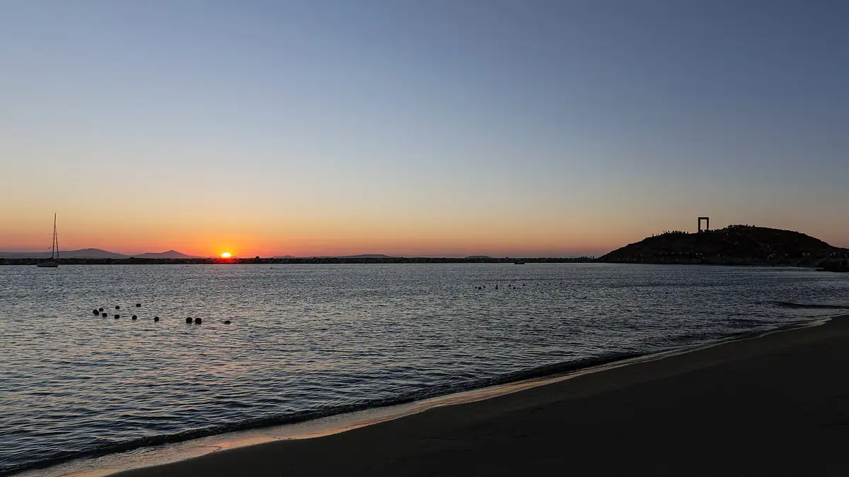 Sunset over the sea at Naxos Town with the Portara stone gate silhouetted on the hill