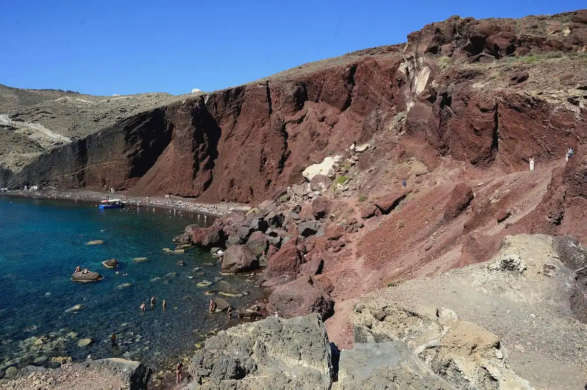 Swimmers and tour boats below the red volcanic cliffs of Red Beach on Santorini