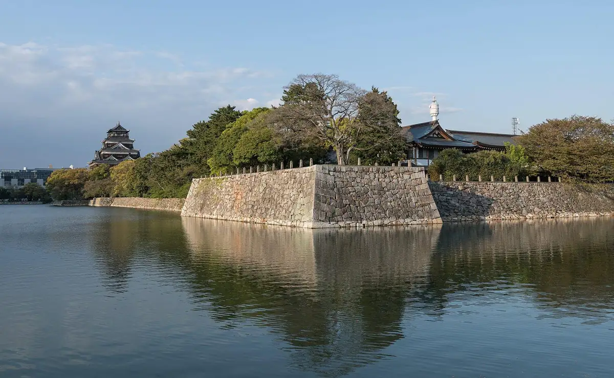 The keep and wide moat of Hiroshima Castle behind sloping stone walls