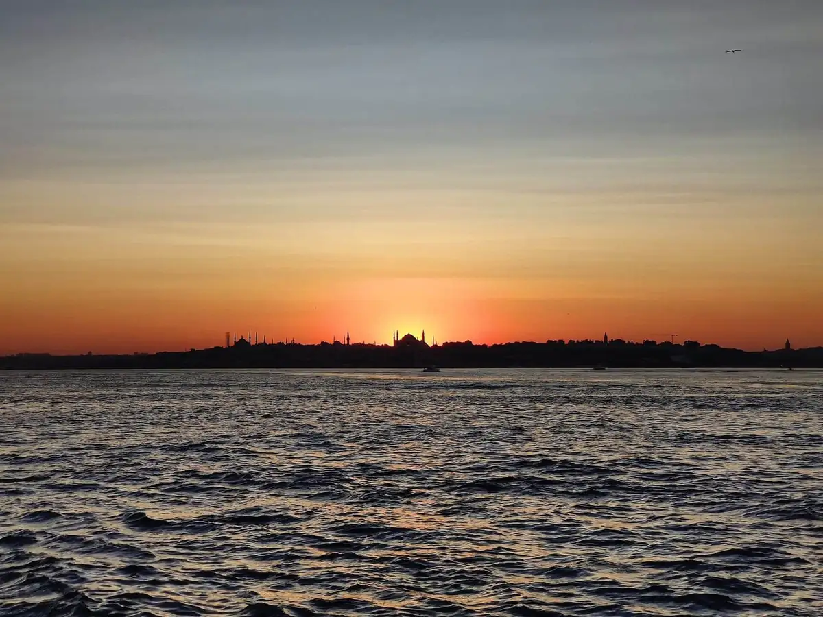 The domes and minarets of the old city silhouetted against an orange sunset over the water