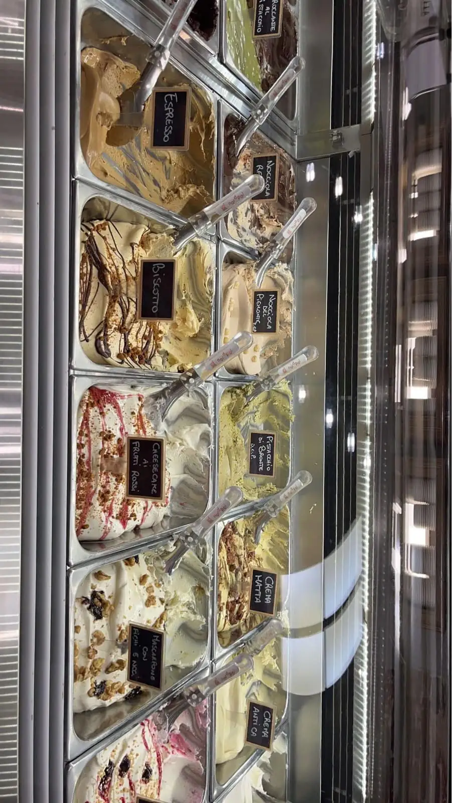 Gelato in flat steel tubs with handwritten flavour labels in an Italian shop