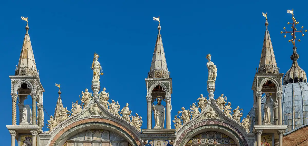 Statues and spires along the upper facade of St Mark's Basilica in Venice against a clear sky