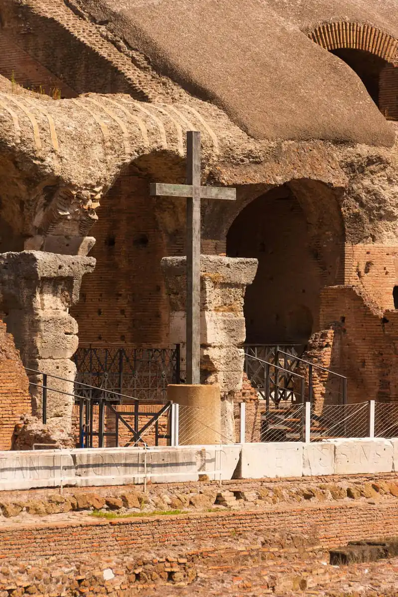 The memorial cross inside the Colosseum arena in Rome, with ancient brick arches behind