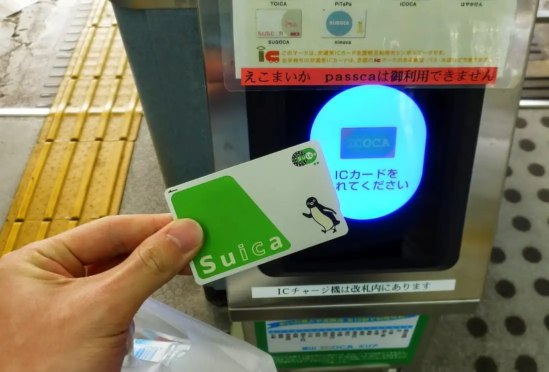 A hand holding a Suica card against an IC reader at a station gate