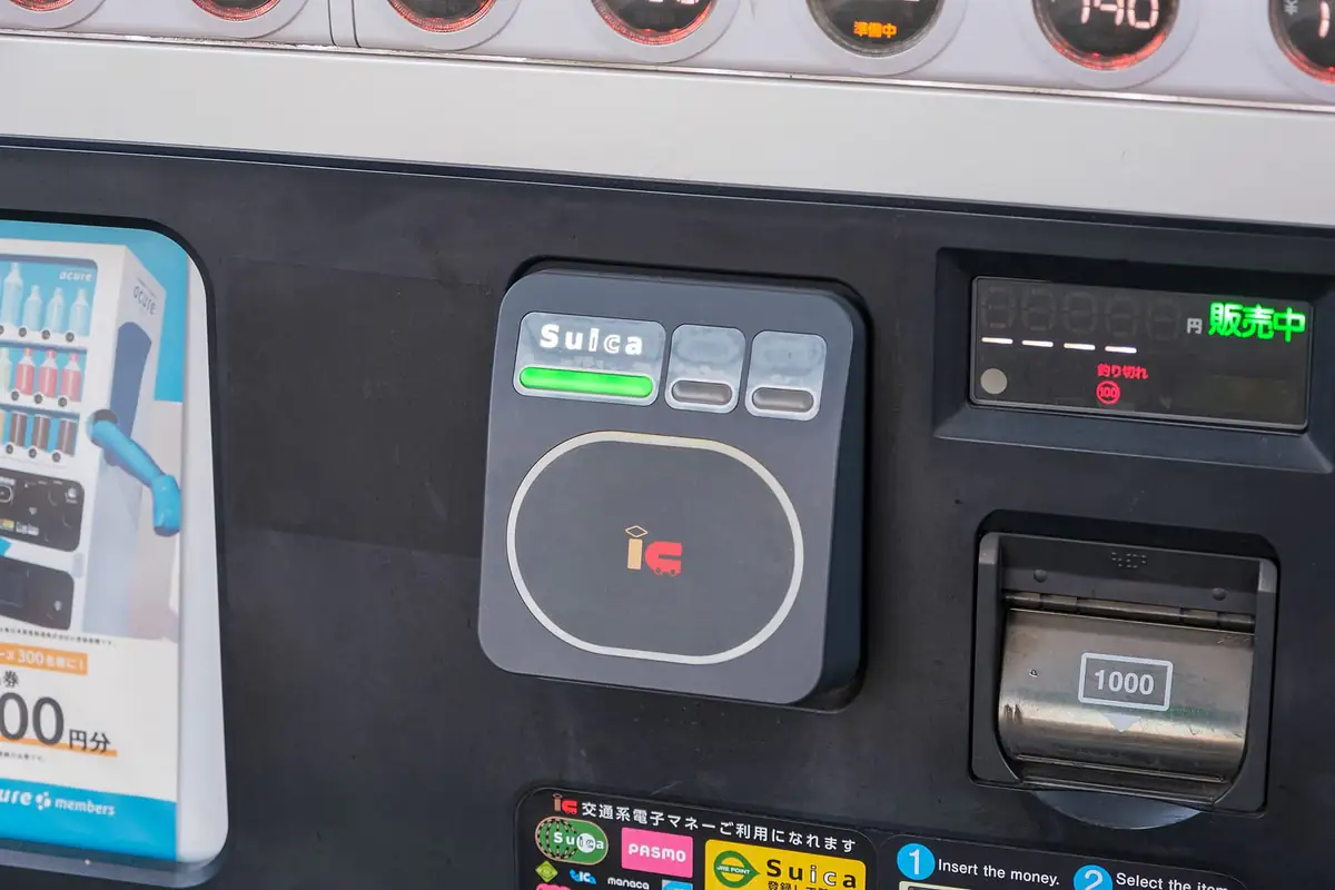 A Suica card being accepted by a vending machine payment panel showing the interoperable IC marks