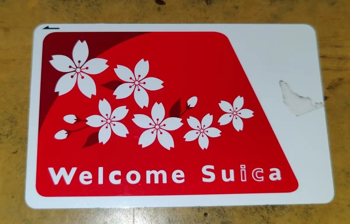 A green Welcome Suica card for overseas visitors held against a blurred station background