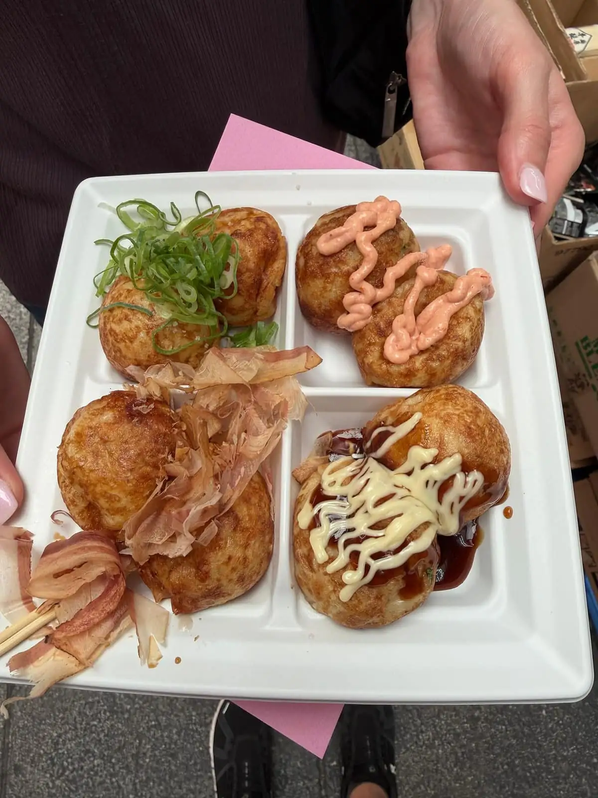 Assorted takoyaki topped with green onions, pink sauce, bonito flakes, sauce and mayonnaise on a divided plate