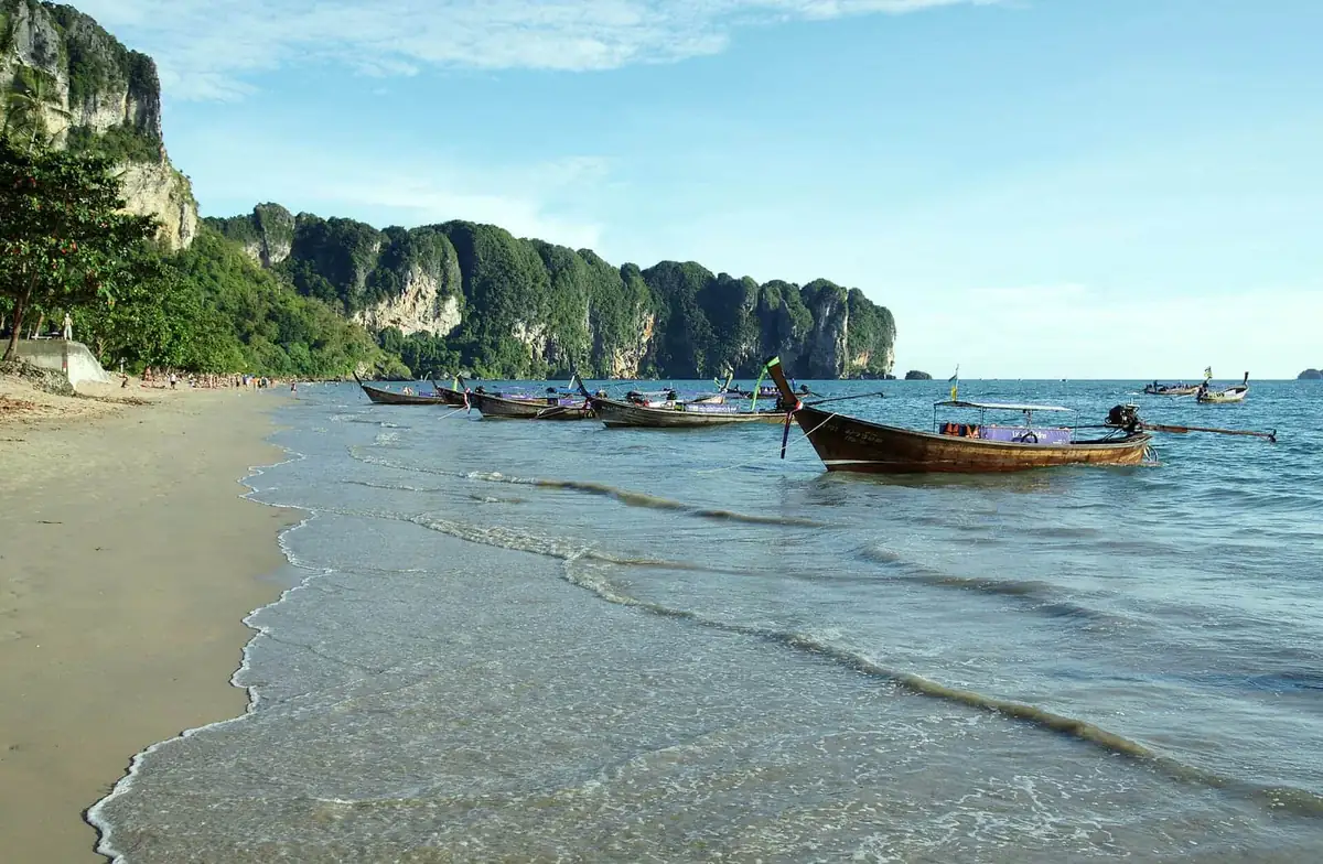 Longtail boats anchored along Ao Nang beach with limestone cliffs rising behind