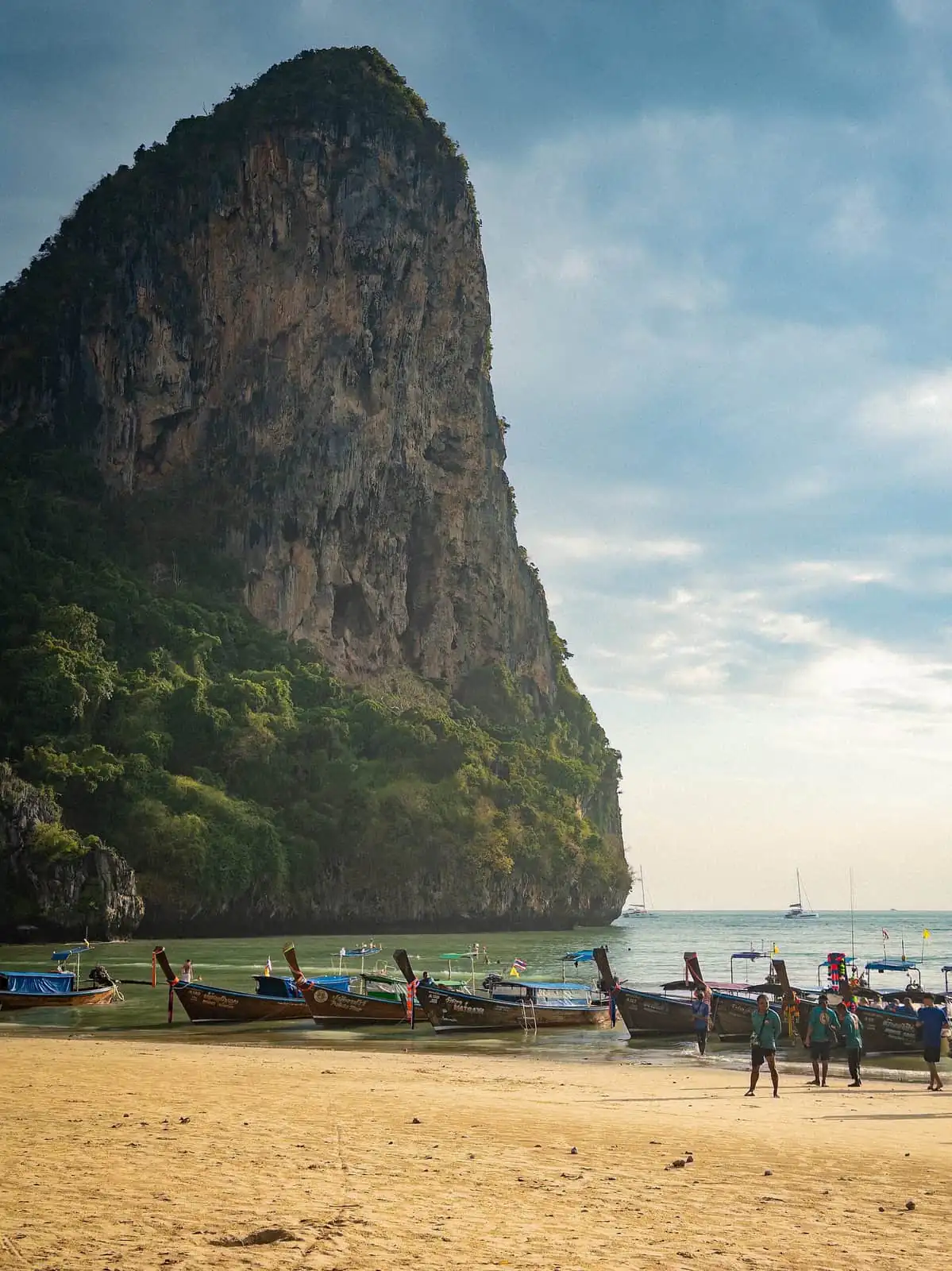A towering limestone karst above longtail boats pulled up on the sand at Railay West Beach