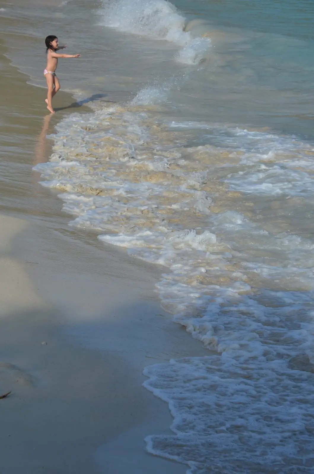 A child playing at the water's edge on the sand at Cala Mondrago