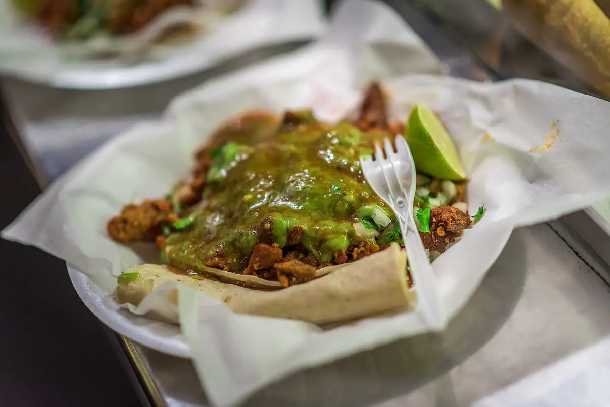 Taco al pastor with green salsa, onion and lime on a paper plate
