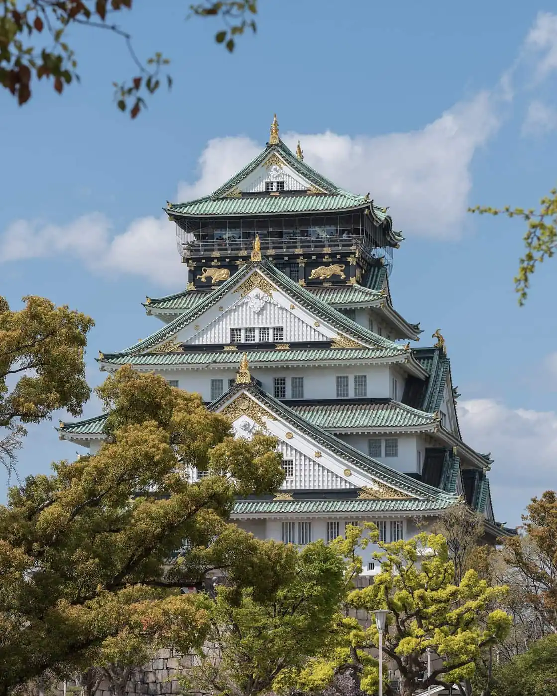 The white and green keep of Osaka Castle rising above trees on a clear day