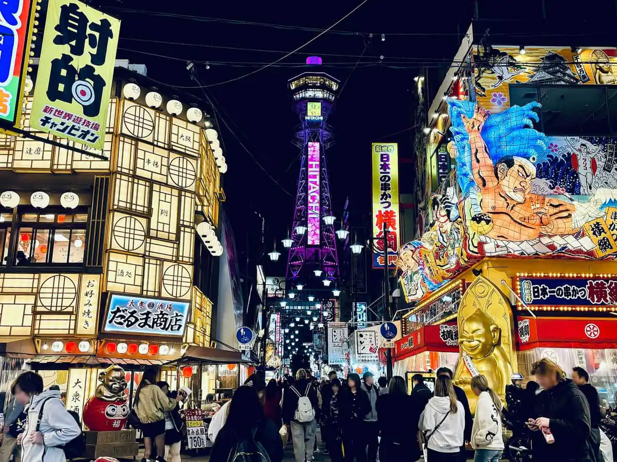 Tsutenkaku Tower lit up at night above the crowded neon streets of Shinsekai