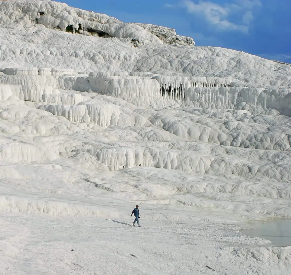 The white travertine terraces of Pamukkale stacked up a hillside, with shallow blue pools along the rim