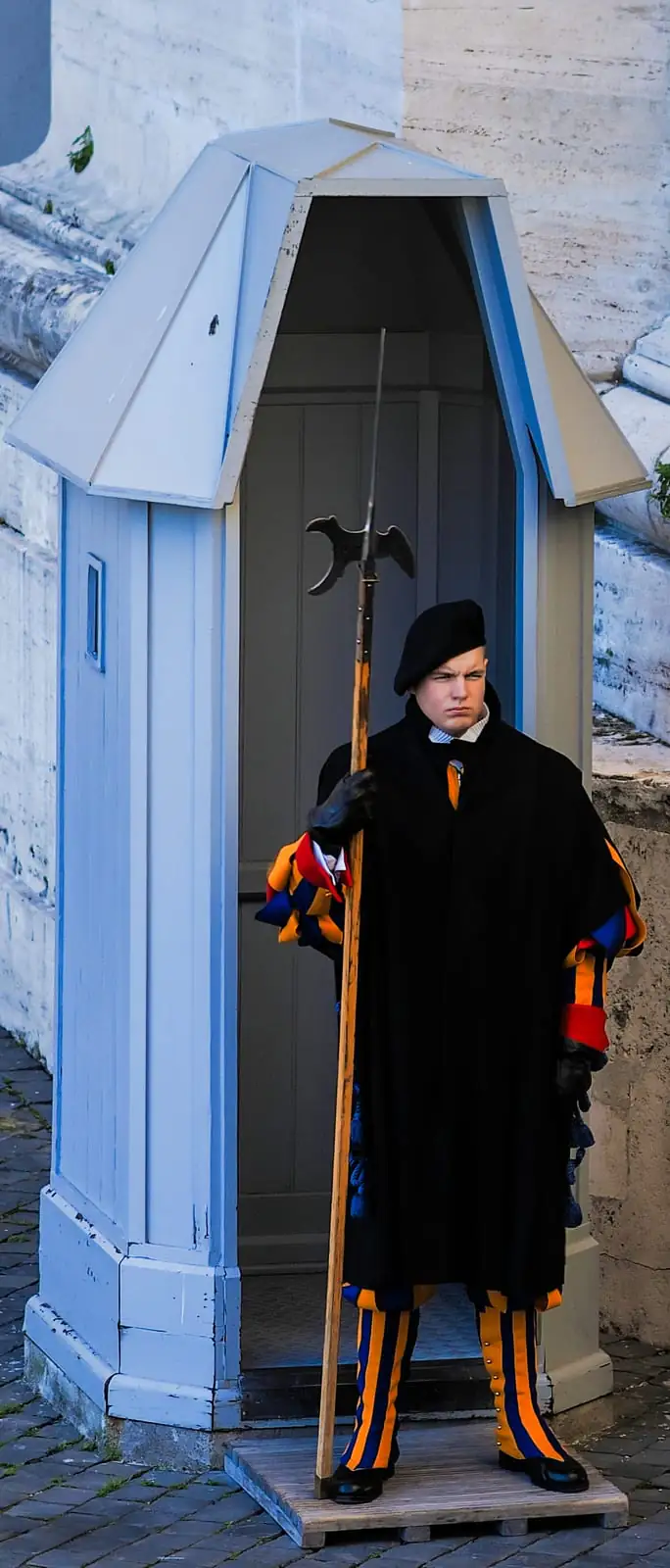 A Swiss Guard in striped uniform standing on duty beside a sentry box at the Vatican