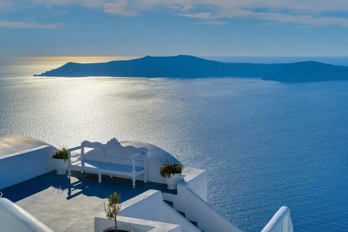 A whitewashed terrace with a bench overlooking the sunlit caldera and the sea at Oia