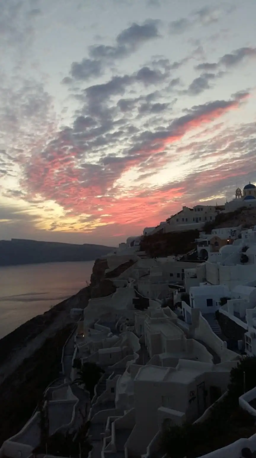 Whitewashed houses of Oia cascading down the cliff at dusk under pink sunset clouds