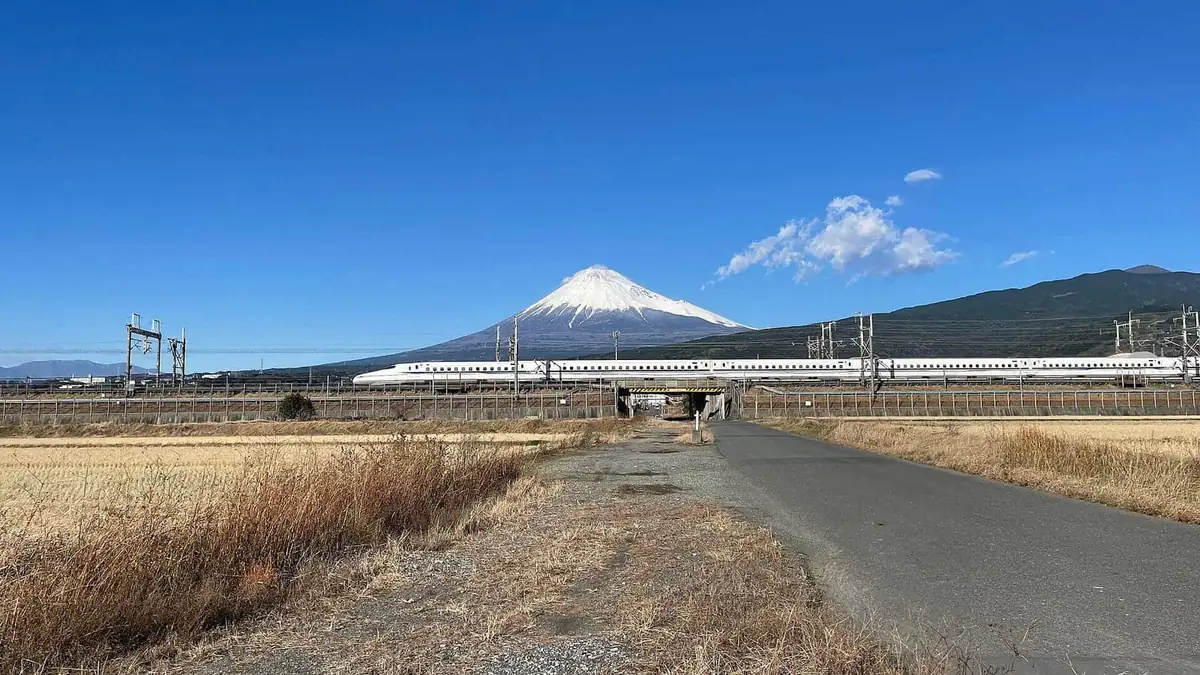 A Shinkansen passing with Mount Fuji behind on a clear day