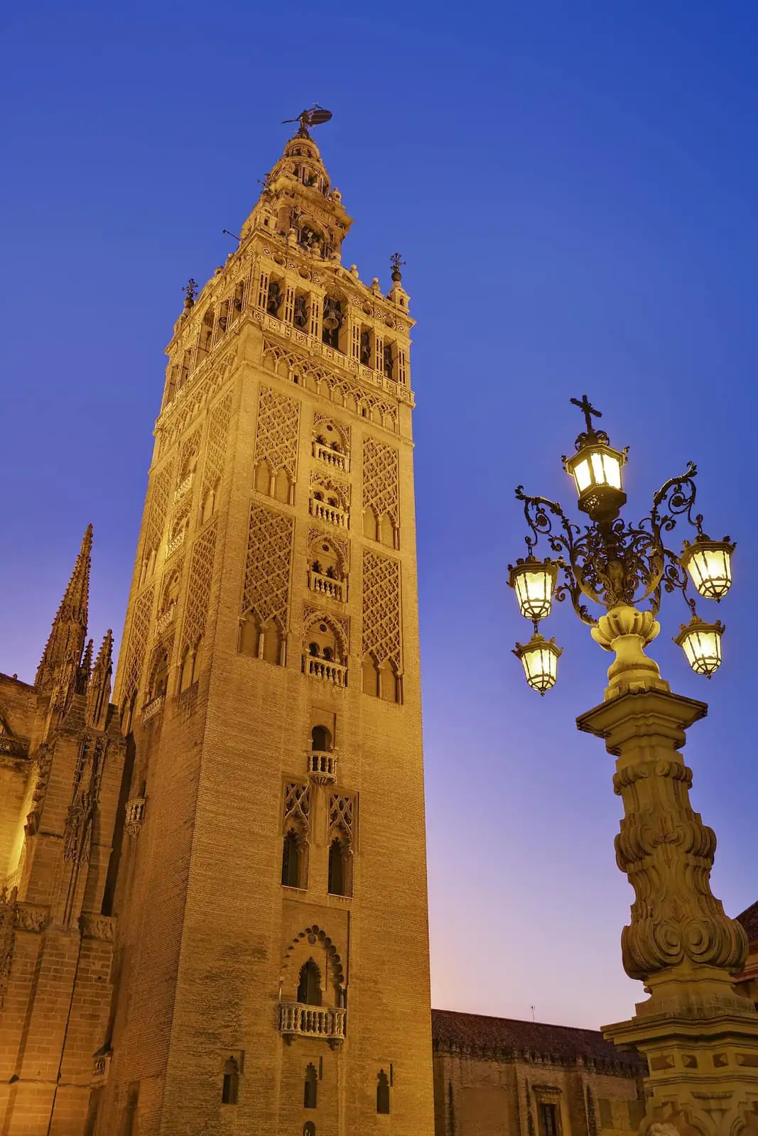 The Giralda tower lit up at dusk, with an ornate street lamp in front