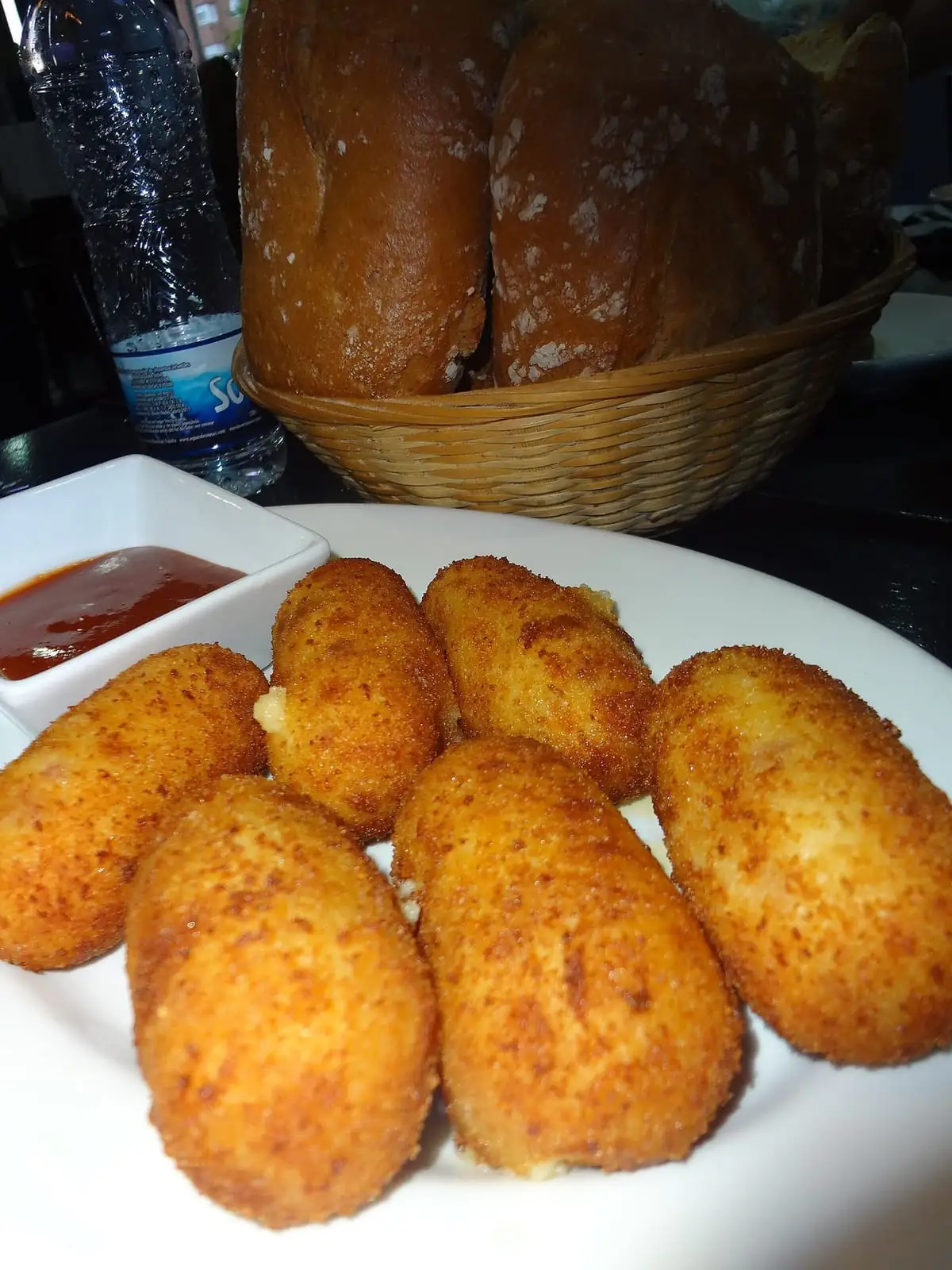 Golden fried croquettes with dipping sauce and a basket of bread rolls on a budget tapas table