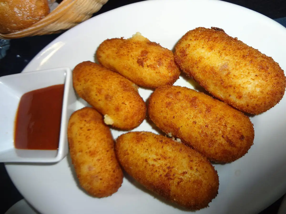 Golden fried croquettes with a red dipping sauce on a white plate at a tapas bar in Madrid