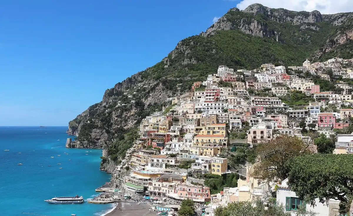 Cliffside houses in Positano rising above the sea, with a ferry near the beach