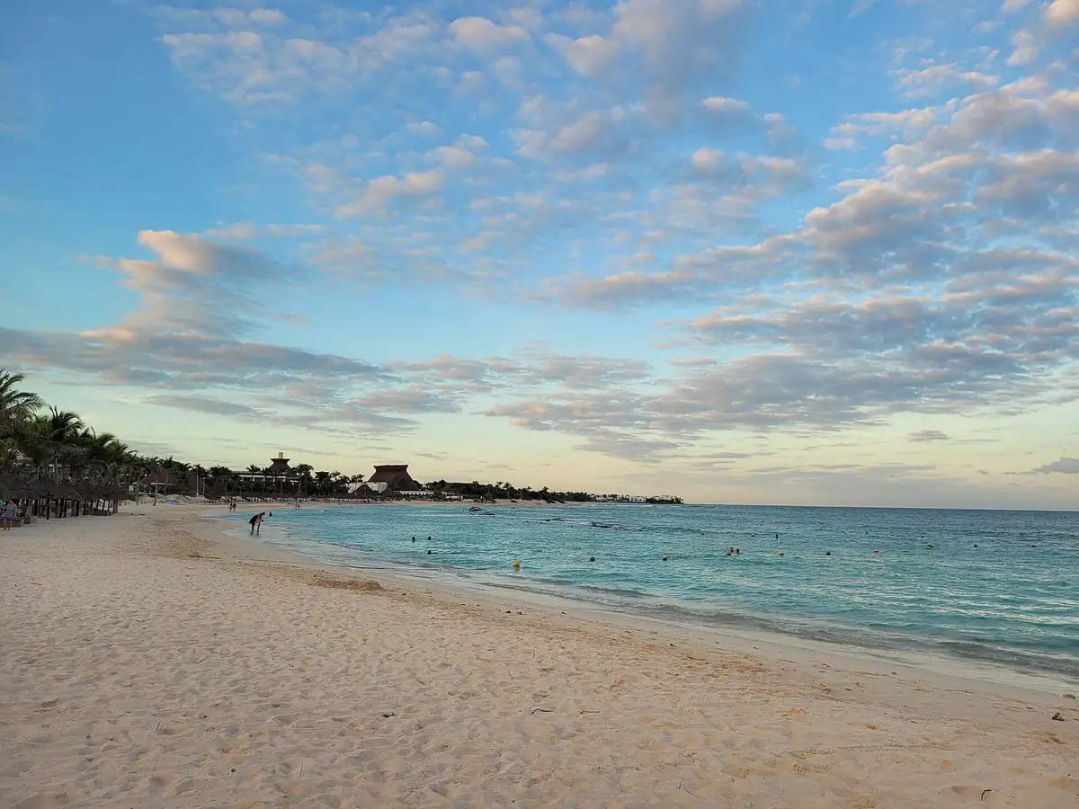 Sunset over a calm beach in the Riviera Maya with palm-thatched palapas along the shore