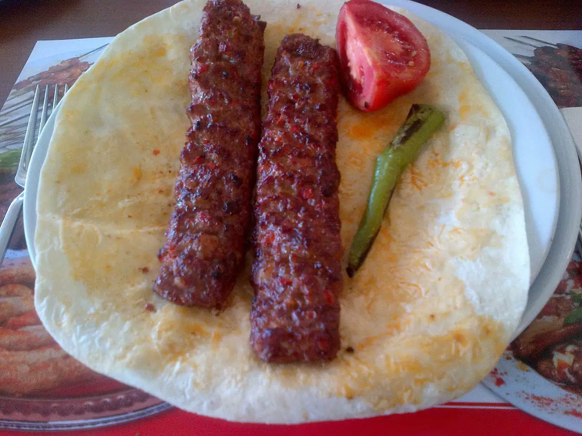 Two Adana kebab skewers on flatbread with tomato and grilled pepper